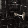 An aluminum swivel tv bracket attached to a bathroom wall in black marble tiles.